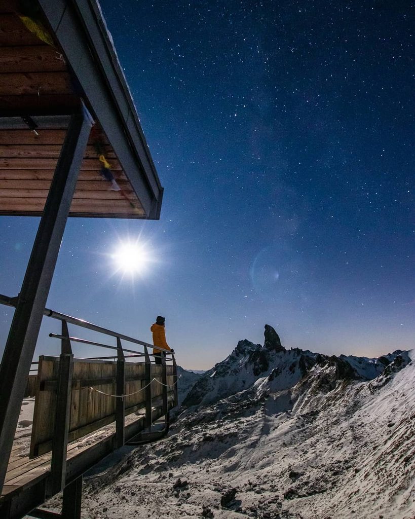 Ciel étoilé et pleine lune au-dessus d'un refuge de montagne enneigé, la nuit